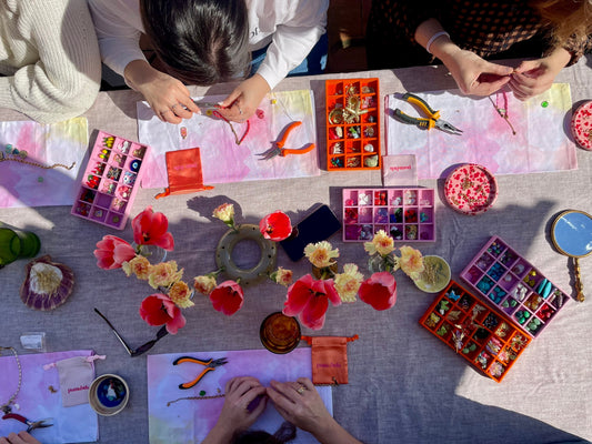Overhead view of a Pamabela necklace-making workshop table with charms, tools and flowers
