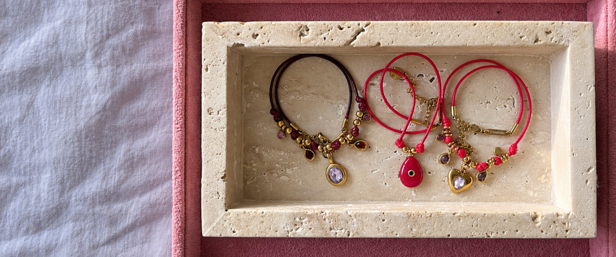 Pamabela handmade cord necklaces with gold charms and crystal pendants in a travertine tray on pink velvet
